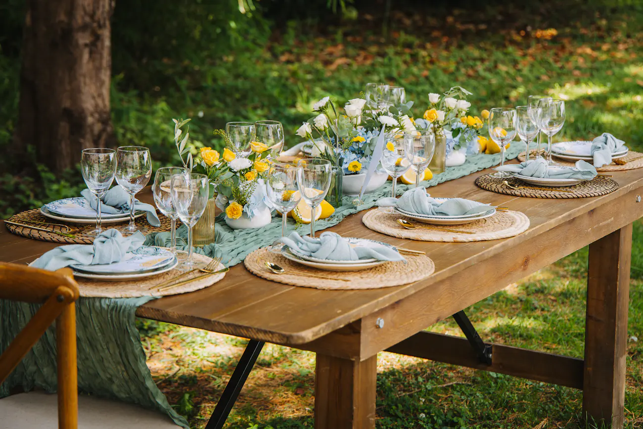 A long outdoor table set with pale blue napkins and yellow flowers